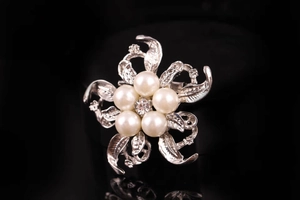 Macro di una spilla a fiore argento con perle bianche e cristallo su uno sfondo nero puro