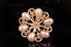 Macro di una spilla dorata circolare con perle a goccia e strass in cristallo lucido