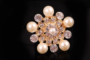 Dettaglio macro della spilla a fiore dorata con perle bianche e strass di cristallo lucidi