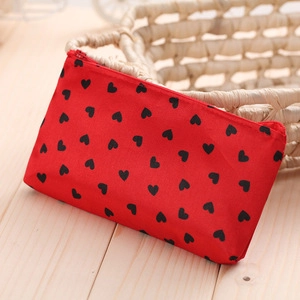 Close-up of red PU travel pouch with black heart pattern and zipper on wooden surface