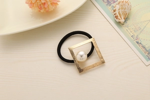 Close-up of golden square metal frame with pearl on black elastic hair tie