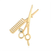 Detailed view of a gold-plated creative scissor and comb brooch with a central white rhinestone