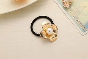 Detail view of elastic hair tie with golden metal flower and large white pearl accent