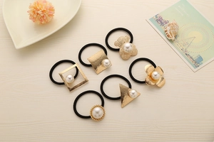 Detail showing elastic hair ties with gold alloy shapes and white pearls on wooden desk