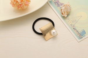 Detail of high-elastic black hair tie with golden square brushed metal and pearl