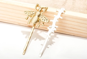 Detailed view of matte gold bee hairpin and silver geometric clip on a wooden stand