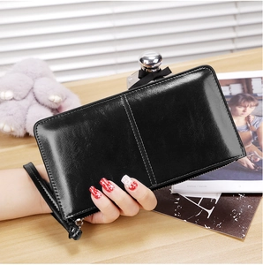 Close-up of black glossy leather long wallet with wristlet strap on a wooden desk