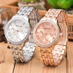 Silver and rose gold Geneva watches with crystal bezels and metal bands on wood