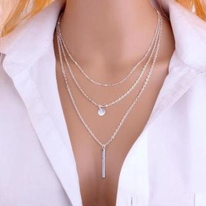 Close-up of triple-layered silver leaf necklace with round and bar pendants on model