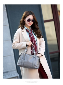 Detail shot of a grey lychee pattern leather Boston bag held by a model in a beige coat