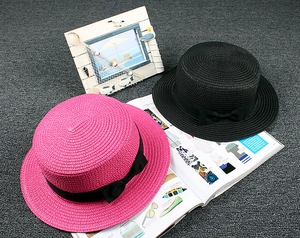 Overhead view of pink and black straw boater hats with black ribbon bows for beach