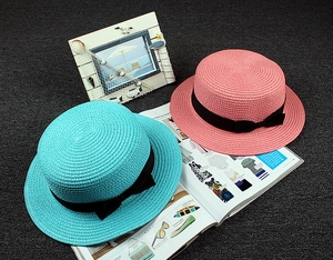 Flat top straw boater hats in blue and pink with black ribbon bows on a textured background