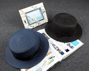 Detail of woven straw texture and black ribbon bow on minimalist flat top summer sun hats