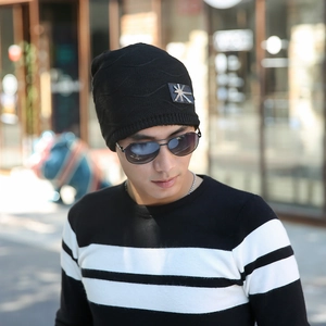 Close-up of black knitted beanie featuring a silver metal logo patch and warm texture