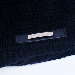 Detail of black knit beanie featuring a leather strap and silver metal 'Fashion' plaque