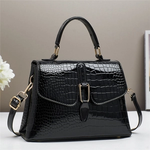 Detail of black crocodile embossed handbag with glossy finish and gold metal hardware