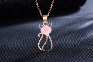 Detail of rose gold cat pendant featuring a polished pink quartz stone on a dark texture