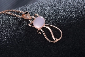 Macro shot of rose gold cat pendant with pink cat eye stone on textured background