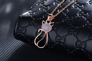 Macro shot of rose gold cat pendant with pink quartz stone on black textured leather