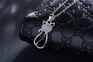 Macro detail of silver cat pendant with pink gemstone on a black textured background