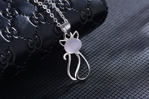 Detail of a silver cat pendant with pink gemstone inlay on a branded leather surface