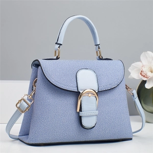 Detail of light blue crossbody bag with denim texture and gold horseshoe buckle
