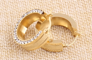 Macro detail of gold stainless steel hoop earrings with frosted finish and inlaid crystals