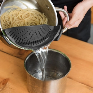 Macro shot of black silicone clip-on pot strainer filtering water from pasta and vegetables