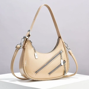Detail shot of beige half-moon bag with decorative diagonal zippers and silver hardware