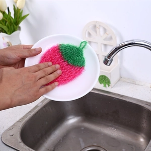 Pink strawberry shaped crochet dishcloth for kitchen cleaning used on a white plate
