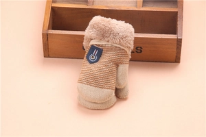 Close-up of children's thick knitted gloves with khaki stripes and plush cuffs on pink background