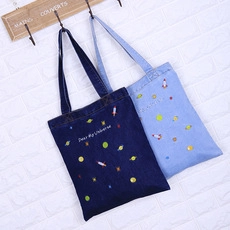 Detail of denim tote bags with embroidered space rockets and planets on brick wall