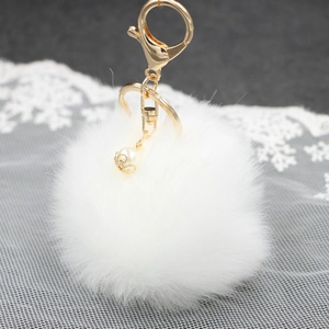 Dettaglio portachiavi a pompon bianco con chiusura dorata e perla su pizzo bianco
