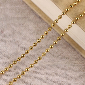 Macro detail of 3.2mm gold ball chain necklace on textured linen and vintage book