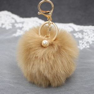 Dettaglio di portachiavi con pompon marrone, chiusura in metallo dorato e decoro con perla