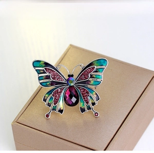 Macro detail of vintage butterfly brooch with green enamel wings and purple teardrop gem