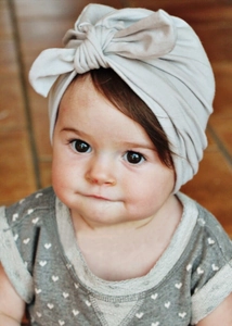 Close-up of a soft light grey cotton baby turban hat with a large bow design on infant