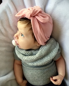 Detail of pink bow turban and grey knit scarf on soft white faux fur background
