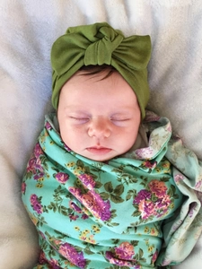 Close-up of baby in olive green knot headband and floral swaddle blanket on soft rug