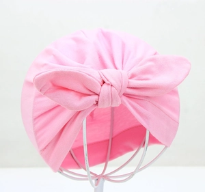 Detail view of pink baby turban hat featuring a large knot bow in soft cotton fabric
