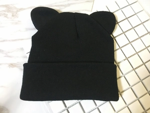 Detail shot of black knitted beanie with cute cat ears design on marble surface