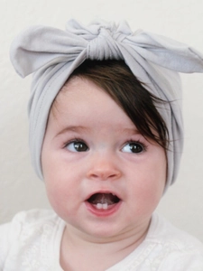 Close-up of baby girl wearing a soft light grey knitted headband with a decorative bow knot