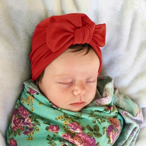 Infant red turban hat with big bow knot accessory for newborn baby on white fluffy blanket