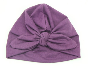 Detail of a purple baby turban hat featuring a decorative bow on elastic knit fabric