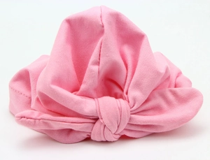 Detail of pink cotton baby turban hat with a knotted bow design on white background