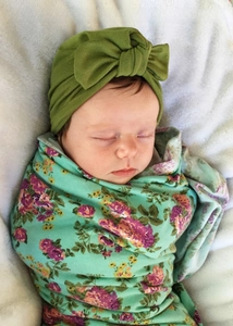 Close-up of baby in turban style knot headband and floral swaddle on soft white plush rug