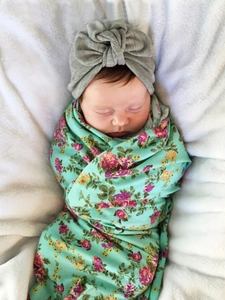 Detailed view of mint floral baby swaddle set with gray bow headband on white plush rug