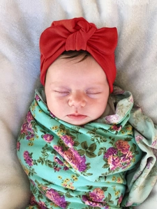 Close-up of baby floral swaddle wrap and red bow headband on soft grey plush background