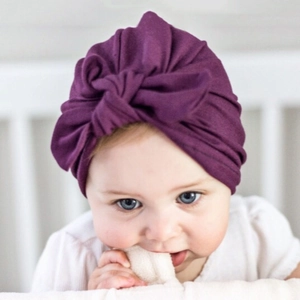 Close-up of deep purple baby turban hat with front knot detail on a newborn infant