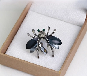 Macro shot of bee brooch with dark crystals and green diamond eyes in a beige jewelry box